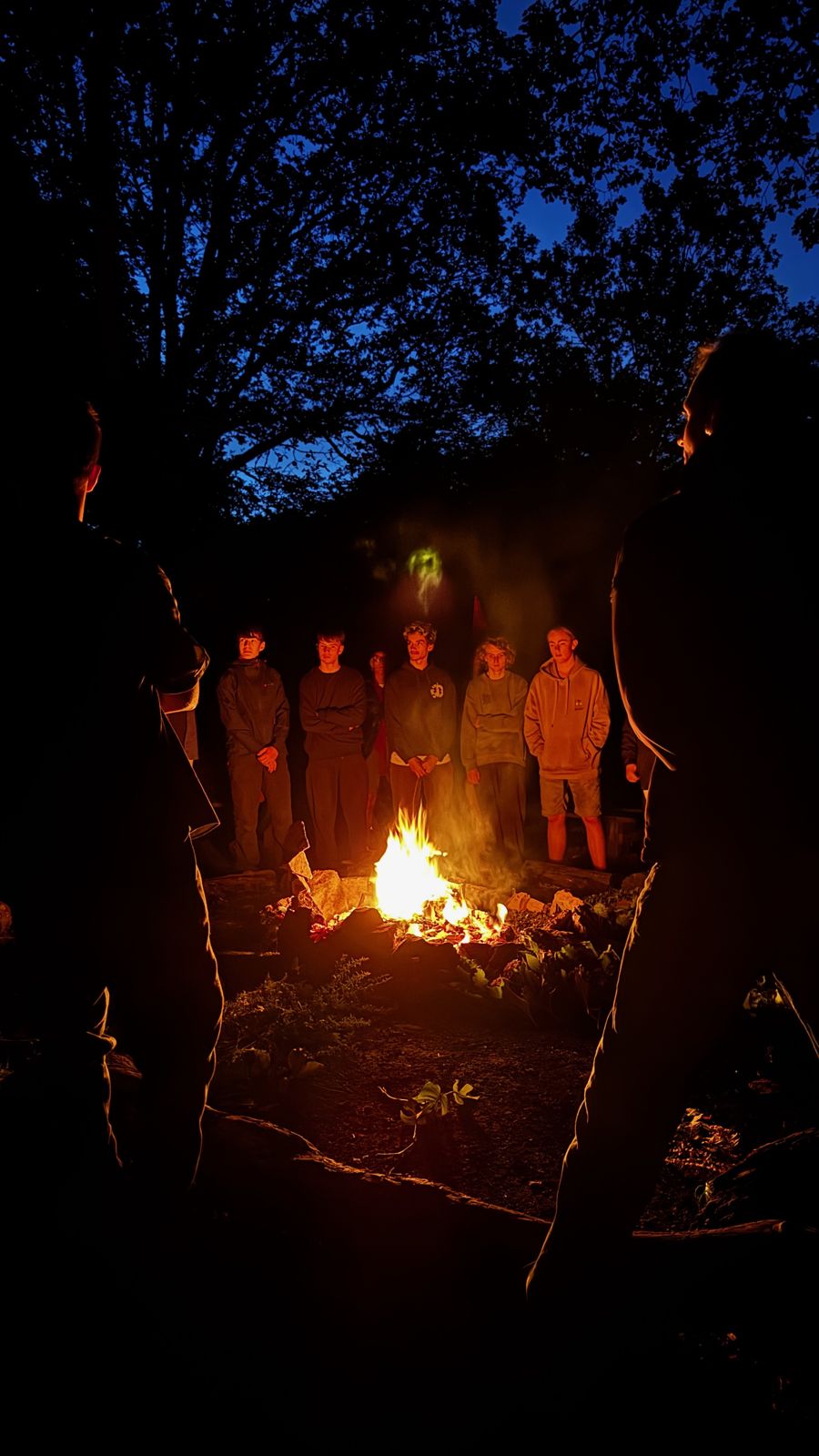 Boys and men standing round the fire at night