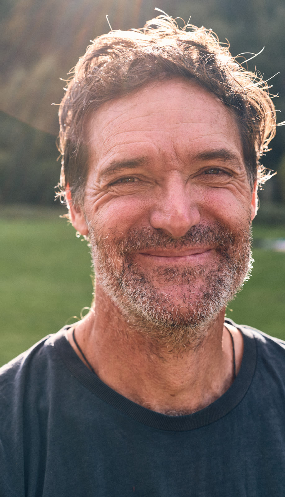 A smiling mentor with stubble, sunlit, in a field